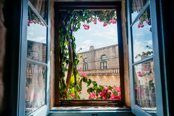 View from old house window with garden flowers and historical building behind. Romantic holidays concept