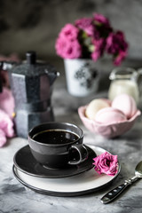 Cup of coffee for Breakfast with marshmallows in the form of macaroon cakes in a black bowl on a dark table and with flowers in a glass