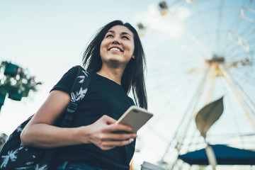 Below view of attractive smiling woman with cellular gadget in hands standing outdoors and laughing...