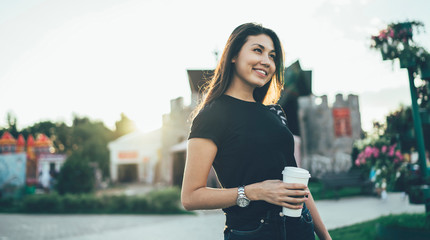 Attractive hipster girl in casual apparel with copy space for brand advertising smiling outdoors during coffee break at street, happy woman with takeaway cup enjoying leisure for recreation