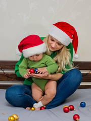 Happy young mother and her daughter in Santa hat plays with Christmas balls.