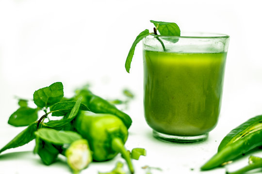 Hot, spicy, tangy and sweet green chili juice in a glass isolated. Horizontal shot of fresh-cut raw green chilis and its juice in a glass bowl on a white surface.Clipping mask.