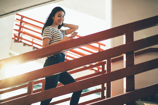 Smiling female blogger climbing outdoors stairs and enjoying online communication with social followers, millennial Asian hipster girl searching online information on public wireless website - Powered by Adobe