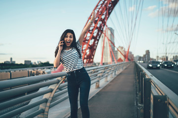 Half length portrait of wonder hipster girl with raised hand satisfied with received news during cellphone communication, excited Asian woman surprised with incoming international phone call
