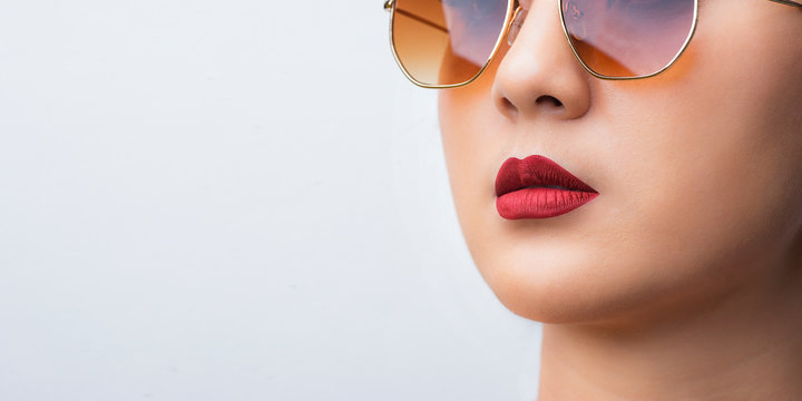 Close up face, Asian woman wearing sunglasses in studio white background. Sexy girl applying cosmetic lipstick make up red color on mouth.