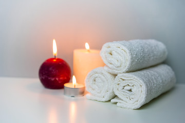 Fototapeta na wymiar SPA and wellness photo with stack of white towels and candles light, horizontal orientation.