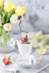 Panna cotta in glass glasses with strawberries on a light background. Bouquet of tulips on a white table.