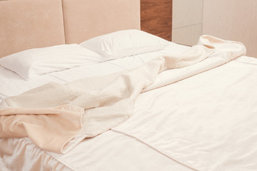 Fototapeta na wymiar Home rest recreation. Empty messy bed with white luxury sheets and wrinkled blanket. Copy space.