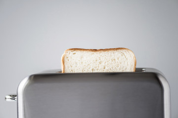 Roasted toast bread popping up of stainless steel retro toaster for breakfast preparation on a gray background.