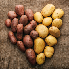 top view of organic raw potatoes arranged in heart on brown rustic sackcloth