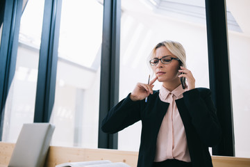 Serious businesswoman in spectacles for provide eyes protection making smartphone call for solving problems via application connected to 4g wireless internet,puzzled female expert talking with partner