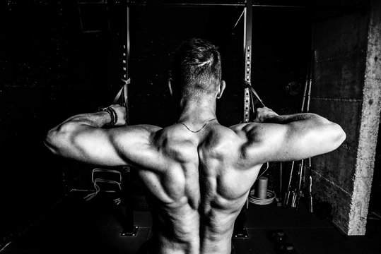 Young muscular fit sweaty strong man doing cross workout training for back muscles in the gym dark image real people black and white