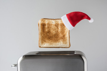Roasted toast bread in a christmas Santa Claus red hat popping up of stainless steel retro toaster...