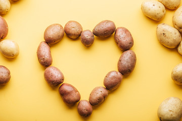 top view of raw whole fresh potatoes arranged in heart on yellow background
