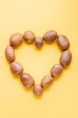 top view of raw whole fresh potatoes arranged in heart on yellow background