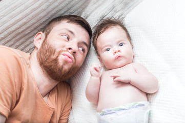 Dad and little son are lying on the bed and grimacing. Close-up portrait. Fatherly love concept
