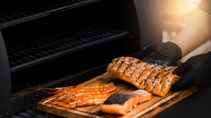 Steakhouse and seafood restaurant. Chef serving smoked salmon fillet and langoustines on wooden board.