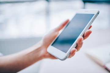 Cropped image of modern smartphone in hand with empty touchscreen, holding new white gadget with contemporary design and advanced application for networking,showing mobile phone with large display.
