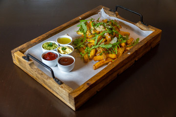 A wooden tray full of fresh fries with rocket salad, parmesan cheese and various dips