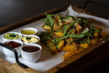 A wooden tray full of fresh fries with rucola salad, parmesan cheese and various dipsA wooden tray full of fresh fries with rocket salad, parmesan cheese and various dips