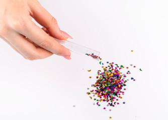 girl sprinkles colored sequins from a jar on a white background