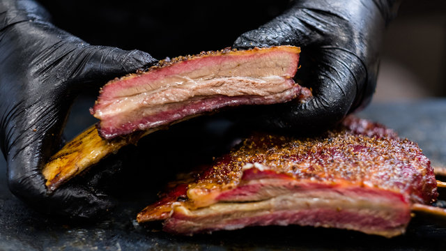Culinary master class. Closeup of chef hands in black cooking gloves holding smoked beef ribs.