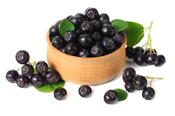 Chokeberry in wooden bowl with green leaves isolated on white background. Black aronia.