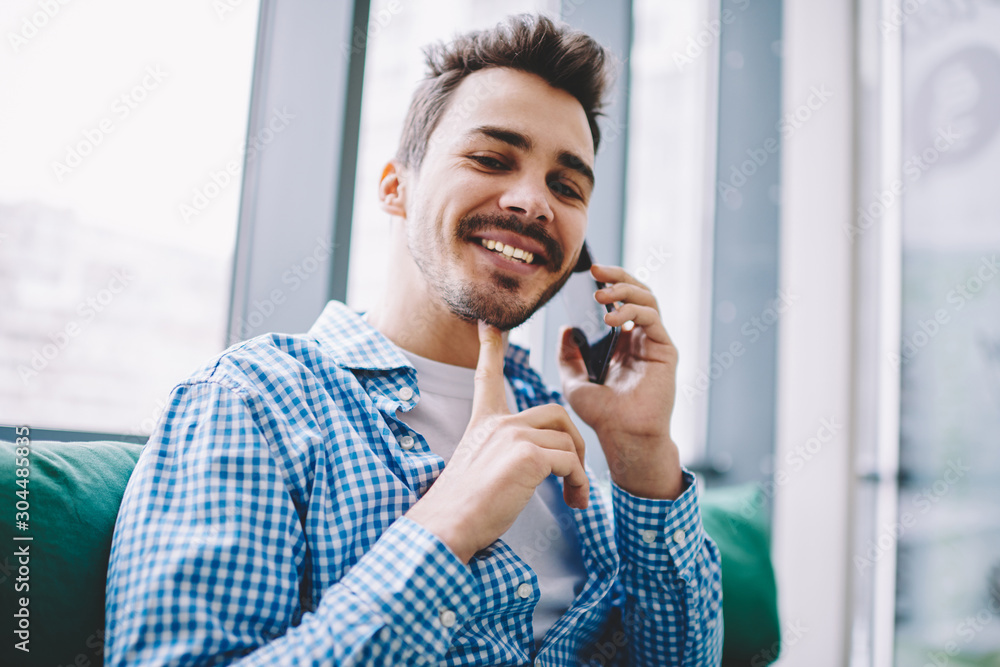 Poster portrait of cheerful hipster guy looking at camera while enjoying break time for making positive sma