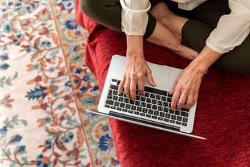 Hands of mature woman using computer at home, top view