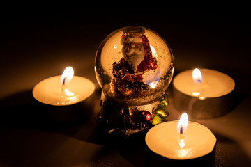 Weihnachtsmann freut sich im Kerzenschein der Adventszeit in seiner Schneekugel auf Heiligabend und die strahlenden funkelnden Kinderaugen am Weihnachtsfest