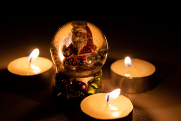 Weihnachtsmann freut sich im Kerzenschein der Adventszeit in seiner Schneekugel auf Heiligabend und...