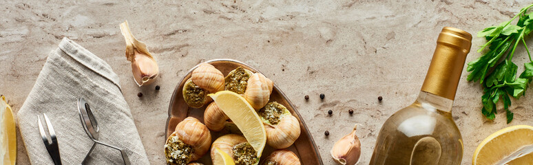 top view of delicious served escargots near bottle of white wine and ingredients on stone background, panoramic shot