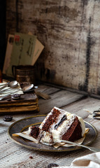 tasty slice of chocolate biscuit cake with white cream, black cookies on vintage metal plate