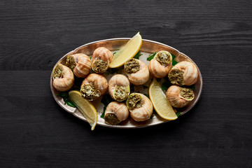 top view of delicious cooked escargots with lemon on black wooden table