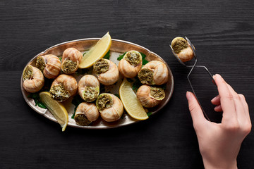 cropped view of woman eating delicious escargots with lemon on black wooden table