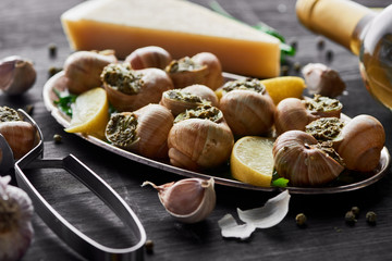delicious cooked escargots with lemon slices on black wooden table with spices and white wine