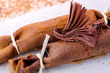 Chocolate russian pancakes, blini with curd filling on the plate. Served with a chocolate figure