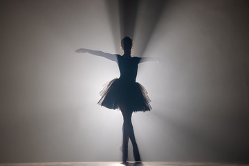 Professional ballerina dancing ballet in spotlights smoke on big stage. Beautiful young girl wearing black tutu dress on floodlights background. Black and white. © kohanova1991