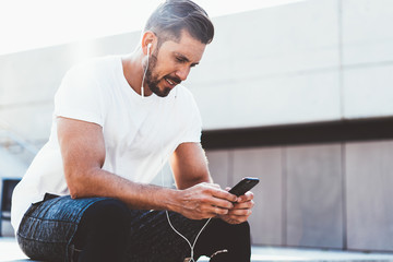 Bearded Caucasian male jogger dressed in stylish sportswear reading received message about success in cardio training connected to 4g wireless on mobile phone, concept of healthy lifestyle