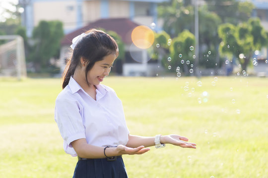 Asian cute girl in a white school uniform is playing a bubble balloon on the lawn. Cute girl is playing soap bubbles in the garden.