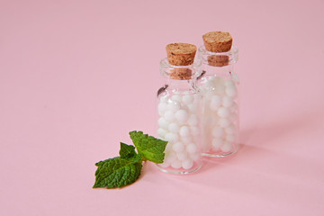 Homeopathic globules and glass bottle close up on pink background. Alternative Homeopathy medicine herbs.