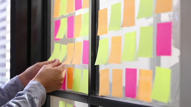 IT worker tracking his tasks on kanban board. Using task control of agile development methodology. Man attaching sticky note to scrum task board in the office
