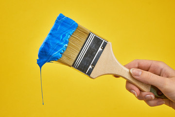 wooden painting brush with blue paint in hand girl on yellow background close up