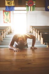 Vertical shot of a male with his head on a wooden surface in the church praying