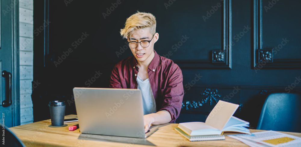 Poster stylish japanese young man sitting at laptop and working remotely in modern space of coworking.chine