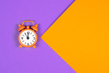 Classic analogue orange alarm clock on double-colored background. Trendy colors in time management concept with copy space for text.