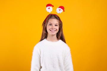 Studio shot of beautiful young girl wearing white knitted sweater, posing over yellow isolated background. Christmas & new year themed portrait of little girl smiling. Close up, copy space, background