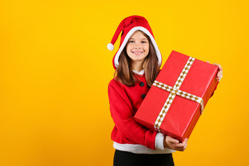 Studio shot of beautiful little girl wearing santa claus hoodie suit, posing over yellow isolated background. Christmas & new year themed portrait of female smiling. Close up, copy space, background.