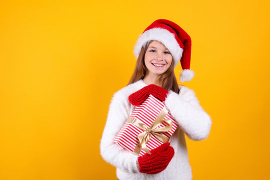 Studio shot of beautiful young girl wearing white knitted sweater, posing over yellow isolated background. Christmas & new year themed portrait of little girl smiling. Close up, copy space, background