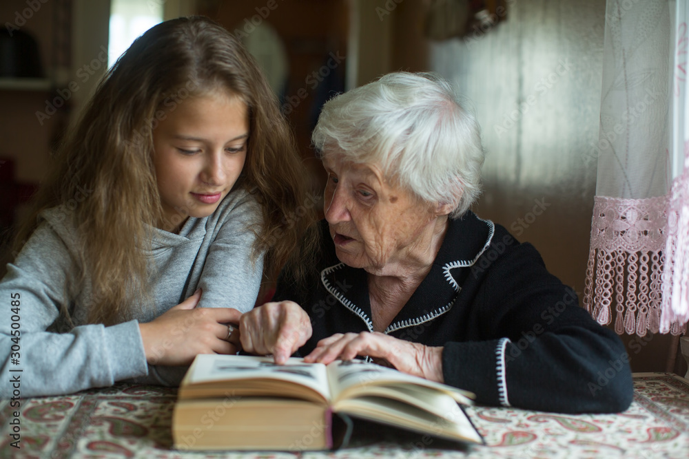 Wall mural cute teen girl with her old great-grandmother reading a book.